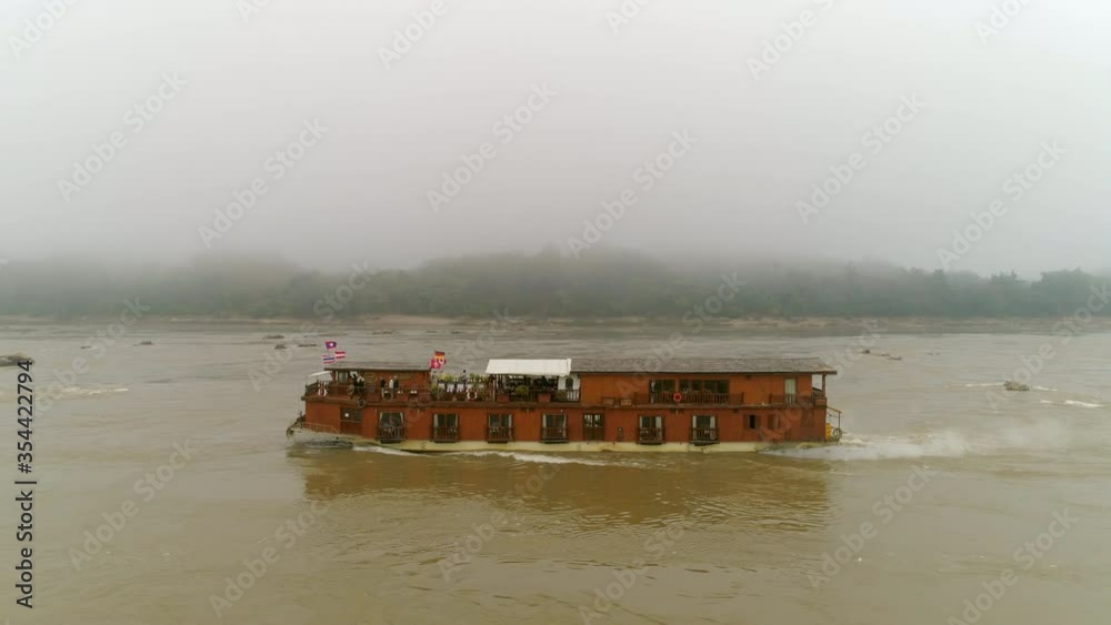 Aerial panning shot of nautical vessel moving in river against sky, drone flying over water in foggy weather - Mekong River, Laos Aerial panning shot of nautical vessel moving in river against sky, drone flying over water in foggy weather - Mekong River, Laos