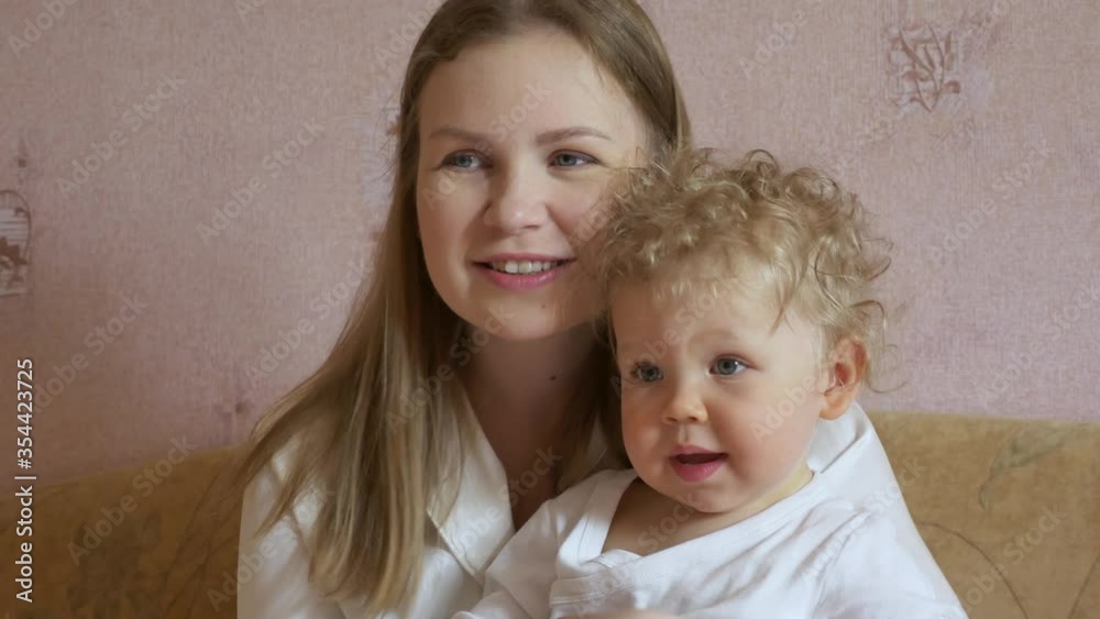 Beautiful attractive mother with a cute baby sits at home on the couch and has fun watching TV. Close-up. Beautiful attractive mother with a cute baby sits at home on the couch and has fun watching TV. Close-up.
