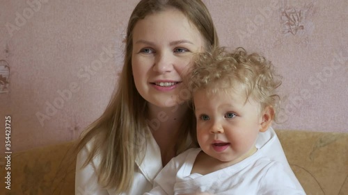Beautiful attractive mother with a cute baby sits at home on the couch and has fun watching TV. Close-up.