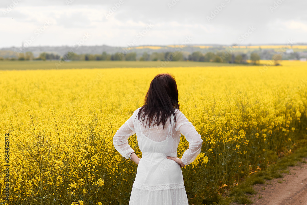 Woman in a white dress standing back in a yellow rapeseed field. Spring concept. Woman in a white dress standing back in a yellow rapeseed field. Spring concept.