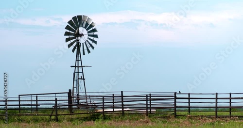 short windmill turning in strong breeze above a cattle corral on prairie summer afternoon