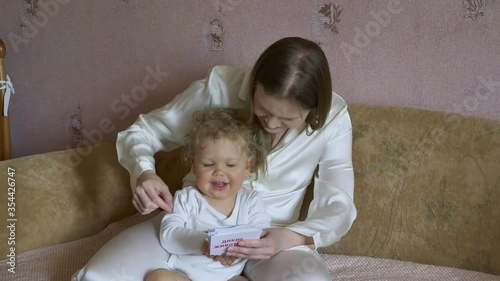 Beautiful attractive mother with a child sitting at home on the couch have fun considering pictures with animals.