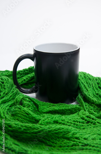 Coffee cup nestled in green lace scarf against a light background. Copy space on the black mug for text or graphics. Lace scarf handknit personal accessory fashion.