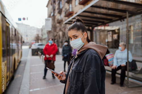 Young woman wearing surgical mask outdoor at bus stop in the street © teksomolika