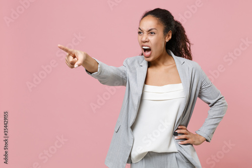 Fotografija Irritated young african american business woman in grey suit white shirt isolated on pink background studio