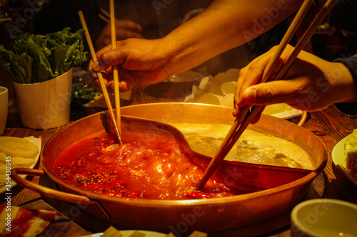 Unrecognized arms taking food with chinese sticks from boiling soup