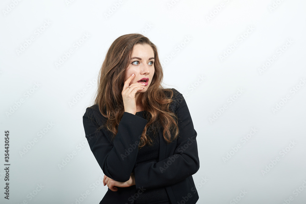 Young Attractive Woman Brunette In In A Black T-Shirt And Sweater On White Background, Focused Female Holds Hand Near Her Face, Smart Person, Thinks, Creates An Idea Young Attractive Woman Brunette In In A Black T-Shirt And Sweater On White Background, Focused Female Holds Hand Near Her Face, Smart Person, Thinks, Creates An Idea