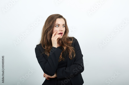 Young Attractive Woman Brunette In In A Black T-Shirt And Sweater On White Background, Focused Female Holds Hand Near Her Face, Smart Person, Thinks, Creates An Idea