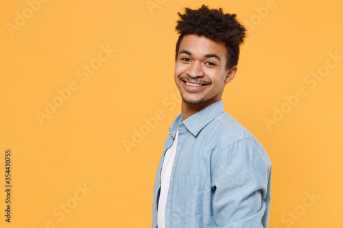 Side view smiling young african american guy in casual blue shirt posing isolated on yellow background studio portrait. People sincere emotions lifestyle concept. Mock up copy space. Looking camera. © ViDi Studio