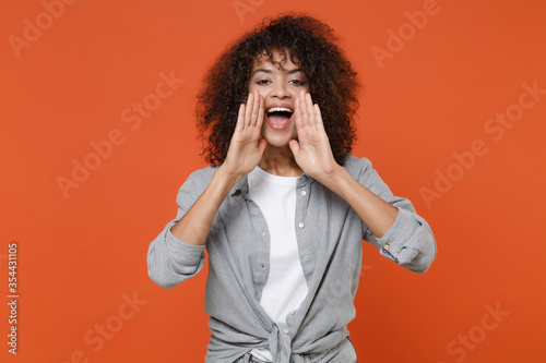 Excited young african american woman girl in gray casual clothes isolated on orange background studio portrait. People lifestyle concept. Mock up copy space. Screaming with hands gesture near mouth.