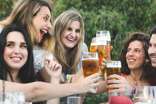 Group of happy friends celebrating and toasting with beer at a bar in summer