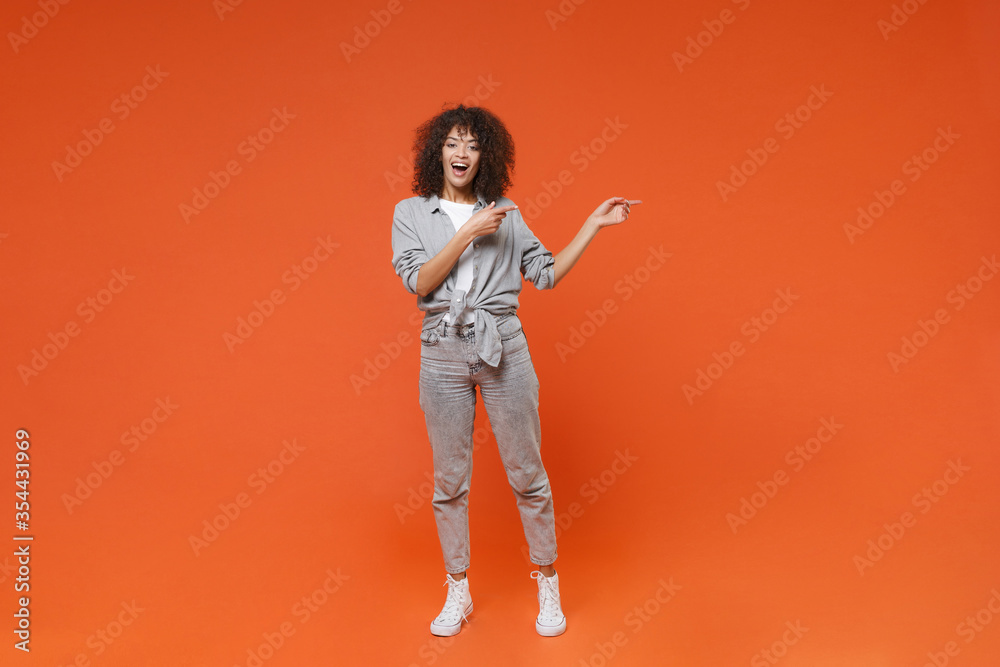 Excited young african american woman girl in gray casual clothes posing isolated on orange background studio portrait. People emotions lifestyle concept. Mock up copy space. Point index fingers aside. Excited young african american woman girl in gray casual clothes posing isolated on orange background studio portrait. People emotions lifestyle concept. Mock up copy space. Point index fingers aside.