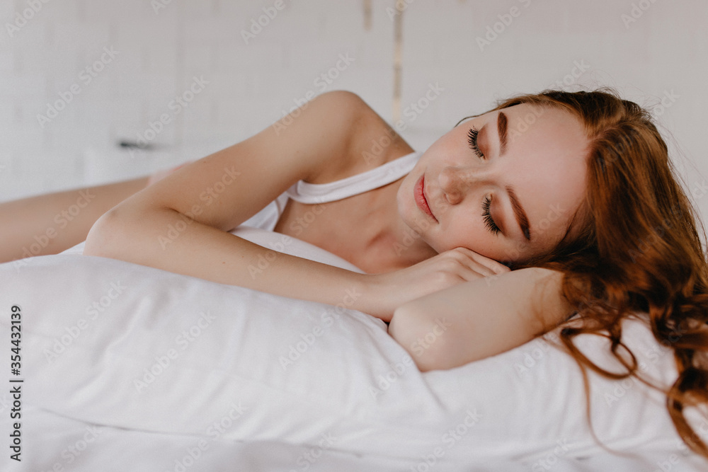 Lovely girl with wavy hairstyle sleeping on pillow. Indoor photo of tired ginger female model with makeup. Lovely girl with wavy hairstyle sleeping on pillow. Indoor photo of tired ginger female model with makeup.
