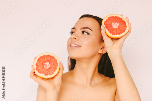 Attractive happy girl with pefrect skin have fun with grapefruit slices and smile isolated on white background. Young beautiful woman posing with healthy citrus fruit. Peeling, beauty treatment, diet photo