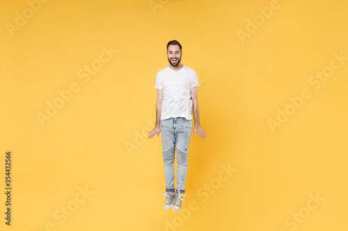 Cheerful young bearded man guy in white casual t-shirt posing isolated on yellow wall background studio portrait. People sincere emotions lifestyle concept. Mock up copy space. Jumping having fun.