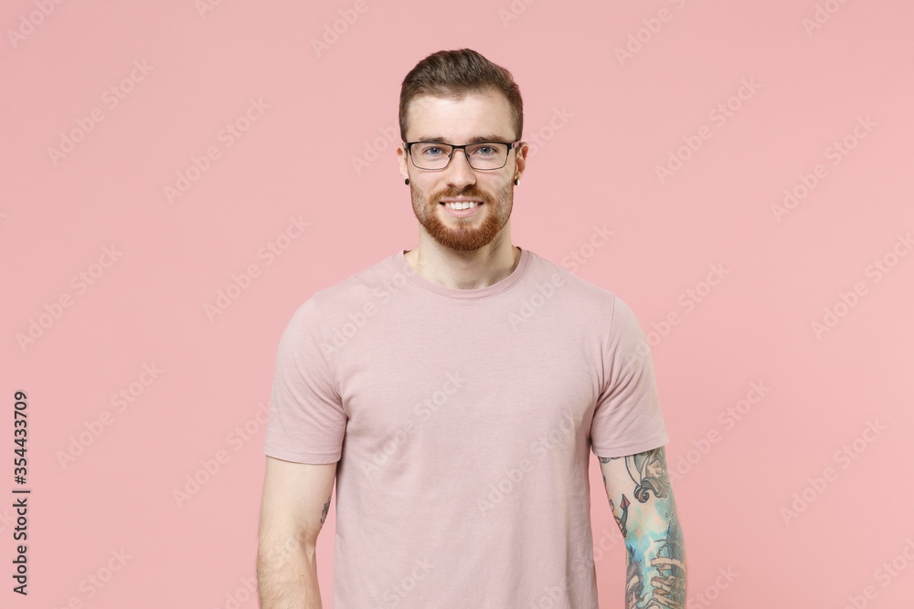 Smiling young bearded tattooed man guy in pastel casual t-shirt, eyeglasses isolated on pink background studio portrait. People sincere emotions lifestyle concept. Mock up copy space. Looking camera. Smiling young bearded tattooed man guy in pastel casual t-shirt, eyeglasses isolated on pink background studio portrait. People sincere emotions lifestyle concept. Mock up copy space. Looking camera.