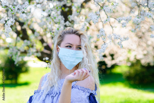 A girl in a protective medical mask in the spring among the blooming garden. . Spring allergy conception