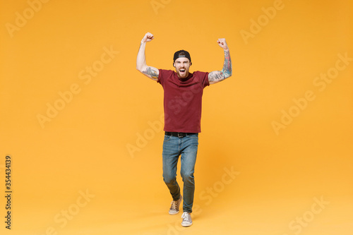 Screaming young bearded tattooed man guy in casual t-shirt black cap posing isolated on yellow background. People emotions lifestyle concept. Mock up copy space. Expressive gesticulating with hands.