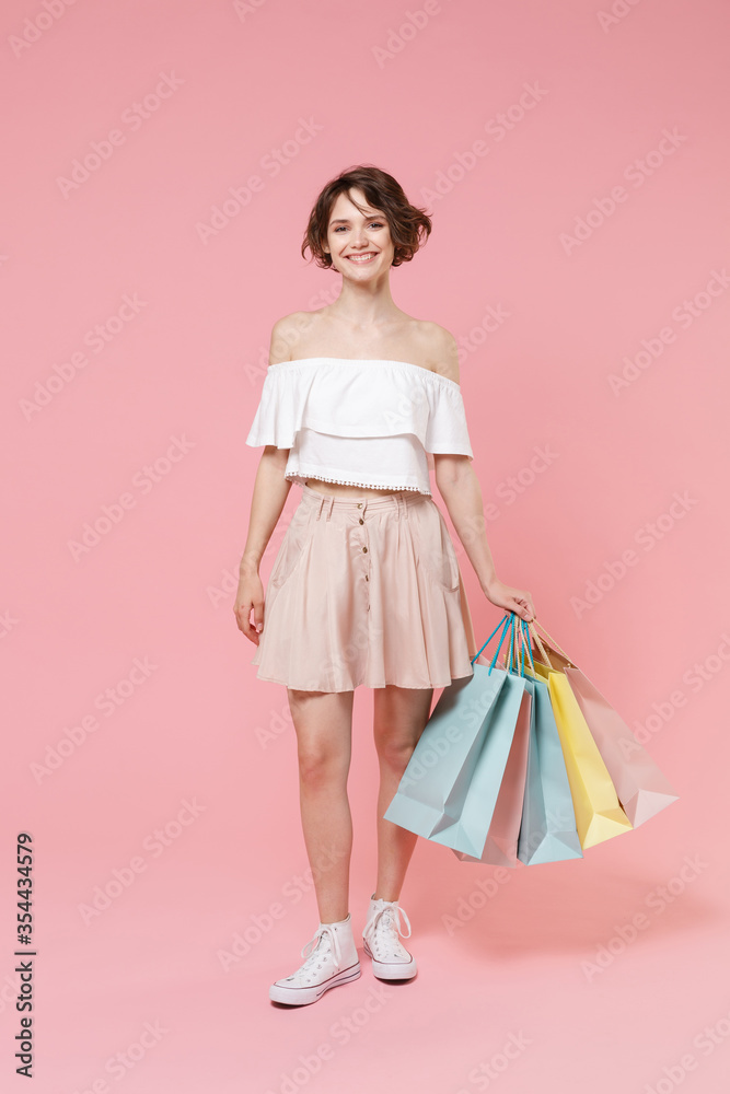 Smiling young woman girl in summer clothes hold package bag with purchases isolated on pastel pink wall background studio portrait. Shopping discount sale concept. Mock up copy space. Looking camera.