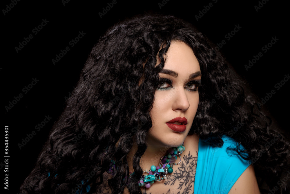 Portrait of an Oriental girl with bright make-up in blue dress and black veil with turquoise jewelry on a dark background. Portrait of an Oriental girl with bright make-up in blue dress and black veil with turquoise jewelry on a dark background.