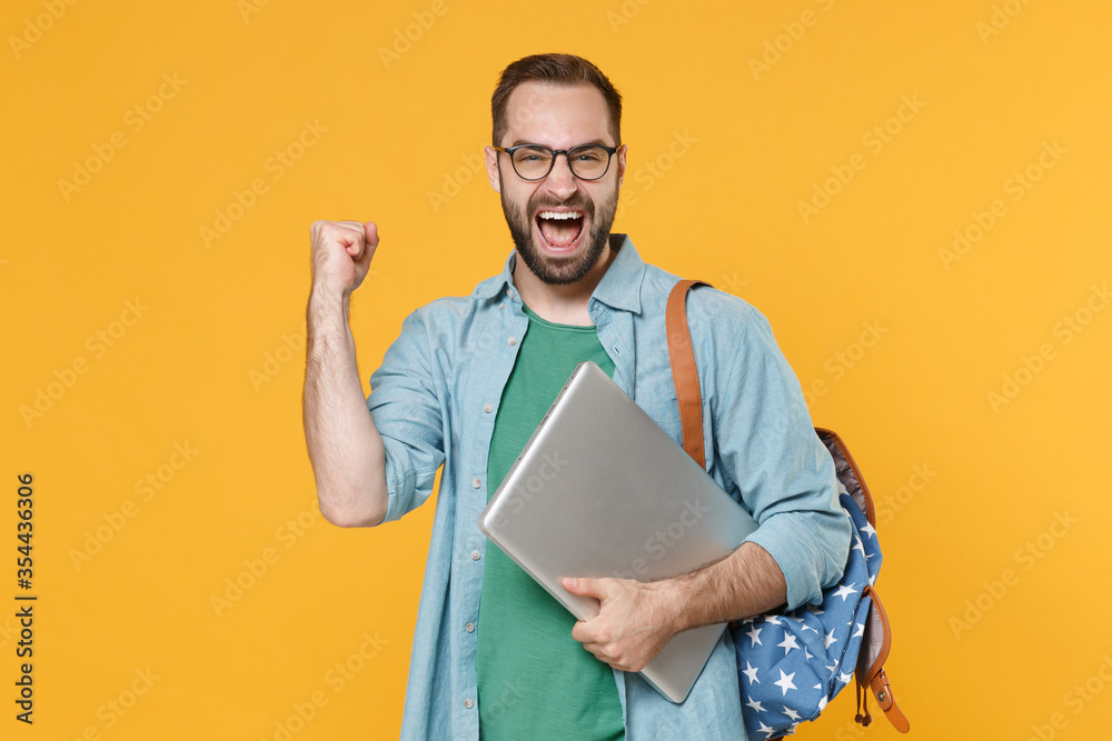 Happy man student in casual clothes glasses backpack isolated on yellow background. Education in high school university college concept. Mock up copy space. Hold laptop computer doing winner gesture. Happy man student in casual clothes glasses backpack isolated on yellow background. Education in high school university college concept. Mock up copy space. Hold laptop computer doing winner gesture.