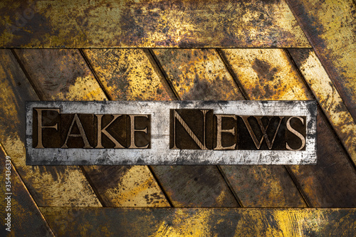 Photo of real authentic typeset letters forming Fake News text on vintage textured silver grunge copper and gold background