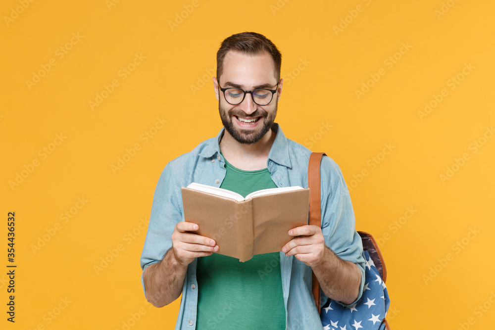 Smiling young man student in casual clothes glasses with backpack isolated on yellow background studio portrait. Education in high school university college concept. Mock up copy space. Reading book. Smiling young man student in casual clothes glasses with backpack isolated on yellow background studio portrait. Education in high school university college concept. Mock up copy space. Reading book.