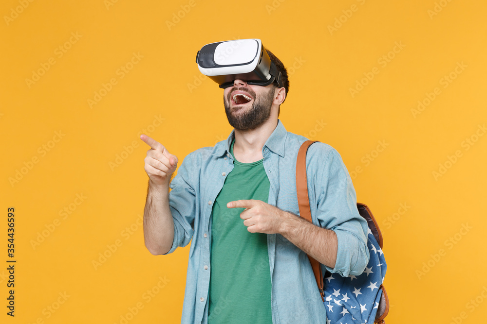Excited young man student with backpack isolated on yellow background. Education in high school university college concept. Mock up copy space. Watching in headset pointing at floating virtual screen. Excited young man student with backpack isolated on yellow background. Education in high school university college concept. Mock up copy space. Watching in headset pointing at floating virtual screen.