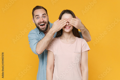 Excited young couple two friends guy girl in pastel blue casual clothes posing isolated on yellow background studio portrait. People lifestyle concept. Mock up copy space. Covering eyes with hands.