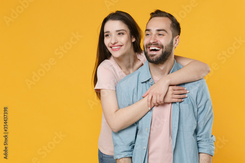 Cheerful young couple two friends guy girl in pastel blue casual clothes isolated on yellow background studio portrait. People emotions lifestyle concept. Mock up copy space. Hugging, looking aside.
