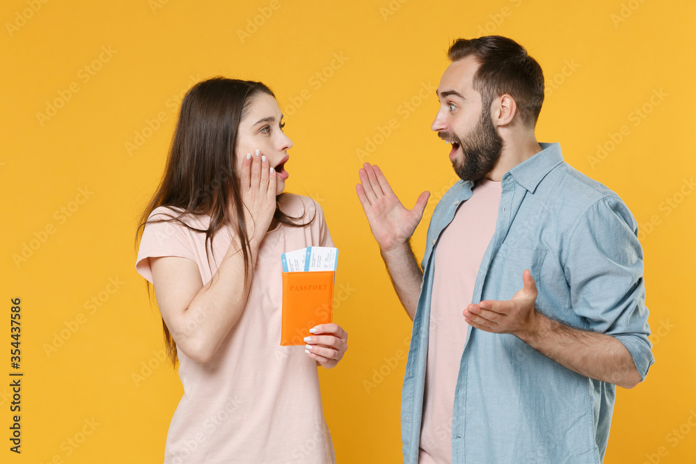Shocked young couple friends guy girl isolated on yellow background. Passenger traveling abroad to travel on weekends getaway. Air flight journey concept. Hold passport tickets, looking at each other. Shocked young couple friends guy girl isolated on yellow background. Passenger traveling abroad to travel on weekends getaway. Air flight journey concept. Hold passport tickets, looking at each other.