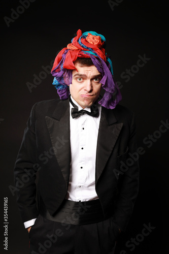 Funny magic man in tuxedo and bow tie with colorful handkerchief isolated on black background