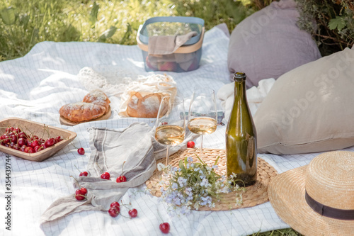 Aesthetic picnic outdoors with wine glasses bread berries and flowers. Rustic picnic with neutral tones colours. 