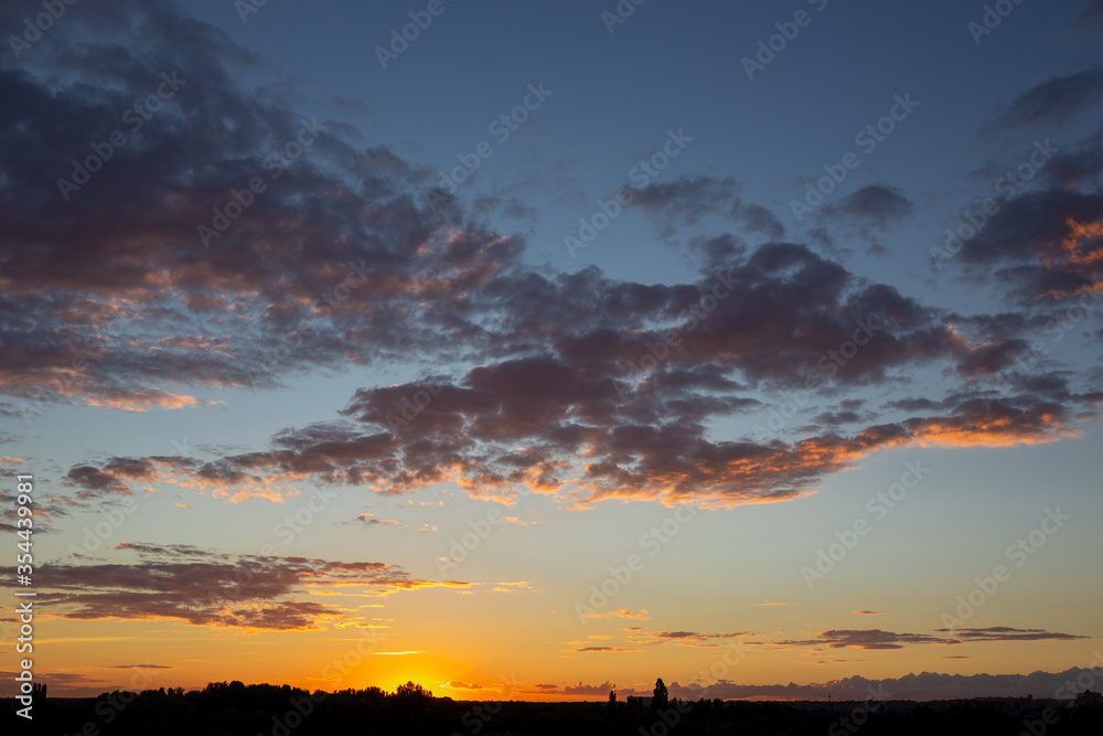 Clouds on a background of blue sky. Beautiful orange sunset.