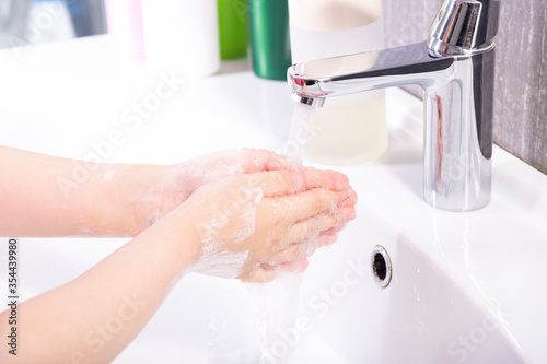 Girl washes her hands with soap under a faucet in a modern bathroom