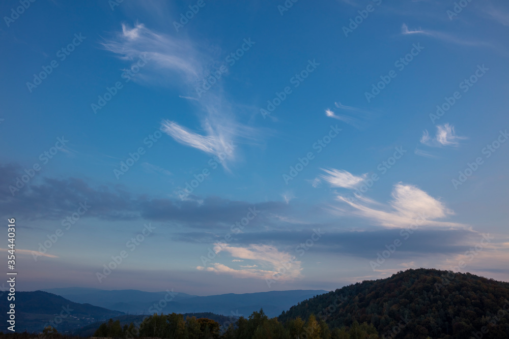 Beautiful white clouds on a background of blue sky. Landscape in the mountains. Sunset sky. Orange sunset.