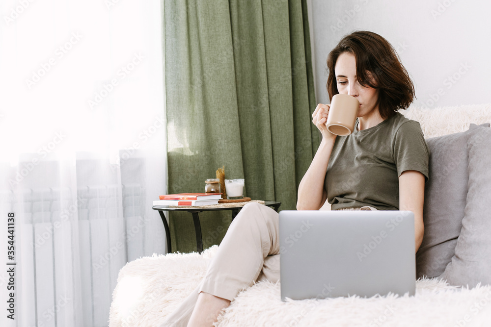 Young woman relaxing and drinking cup of hot coffee or tea using laptop computer in the bedroom. woman checking social apps, doing online shopping and working. Communication and technology concept Young woman relaxing and drinking cup of hot coffee or tea using laptop computer in the bedroom. woman checking social apps, doing online shopping and working. Communication and technology concept