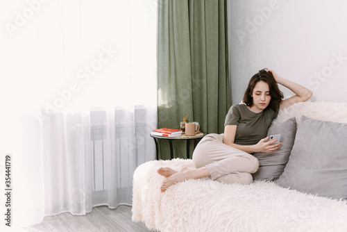 Communication and coziness concept. Happy housewife using a mobile phone sitting on a couch at home