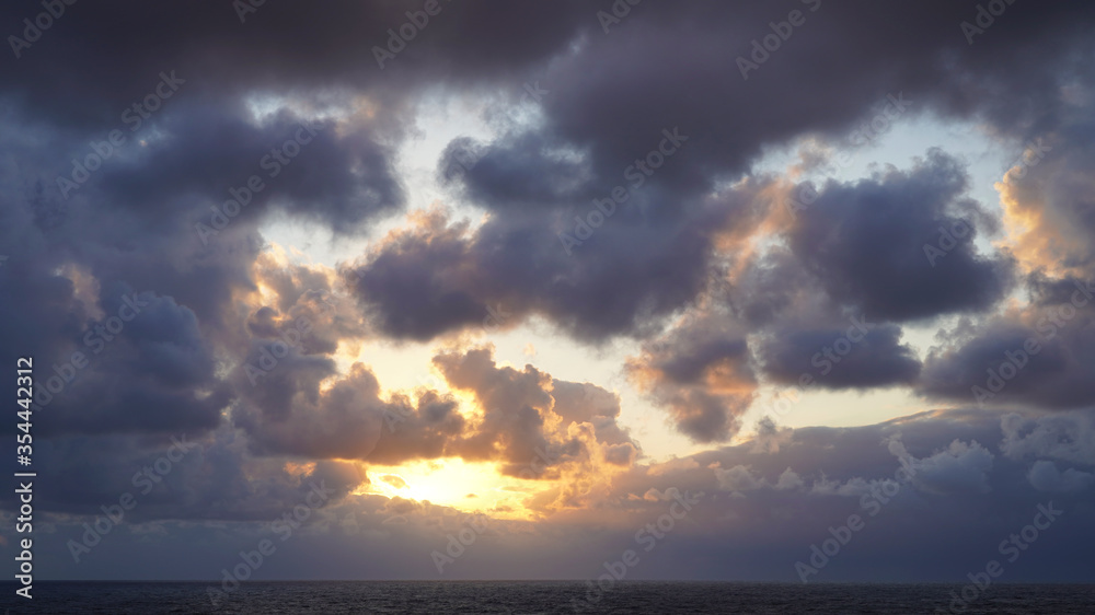Panorama of the sunset sky pierced by the bright rays of the sun in cloudy weather. Beautiful sunset, dawn over the ocean