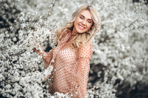 Woman with gorgeous smile  curly blond hair in red dress having fun in blooming garden