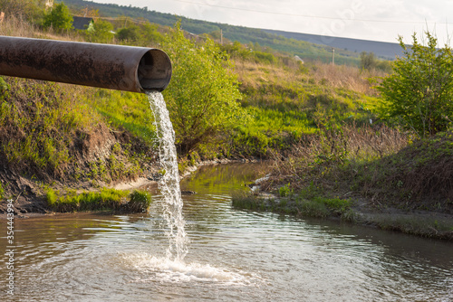 water flows from a pipe into a river against the backdrop of nature. The concept of nature pollution, the release of waste into the water