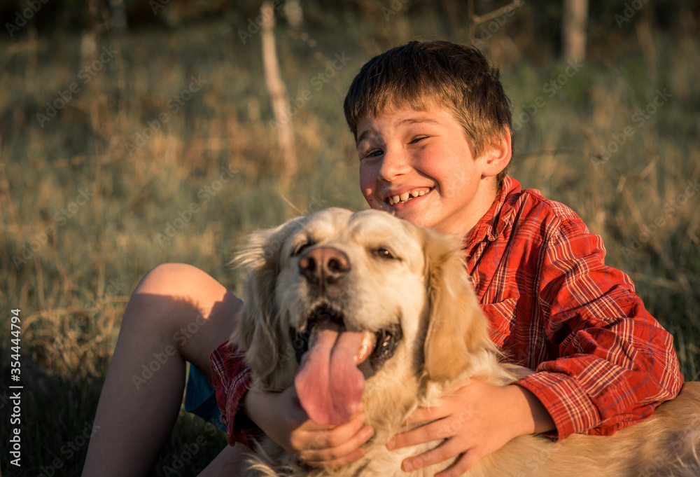 smiling boy and Golden retriever dog outside on the grass on a background of green nature. Image of handsome young man with labrador outdoors. Man on a green grass with dog.