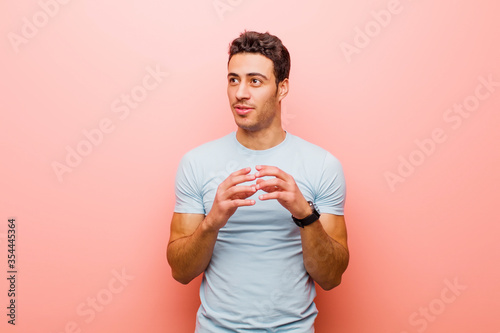 young arabian man scheming and conspiring, thinking devious tricks and cheats, cunning and betraying against pink wall