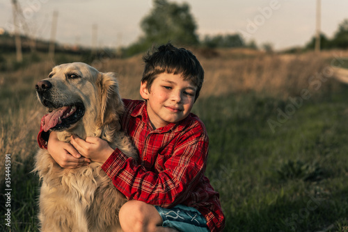 smiling boy and Golden retriever dog outside on the grass on a background of green nature. Image of handsome young man with labrador outdoors. Man on a green grass with dog.