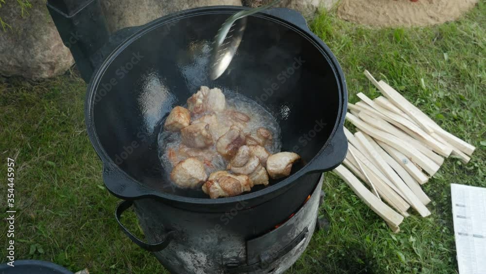 Cooking process, frying pork meat in large cauldron on open fire Cooking process, frying pork meat in large cauldron on open fire