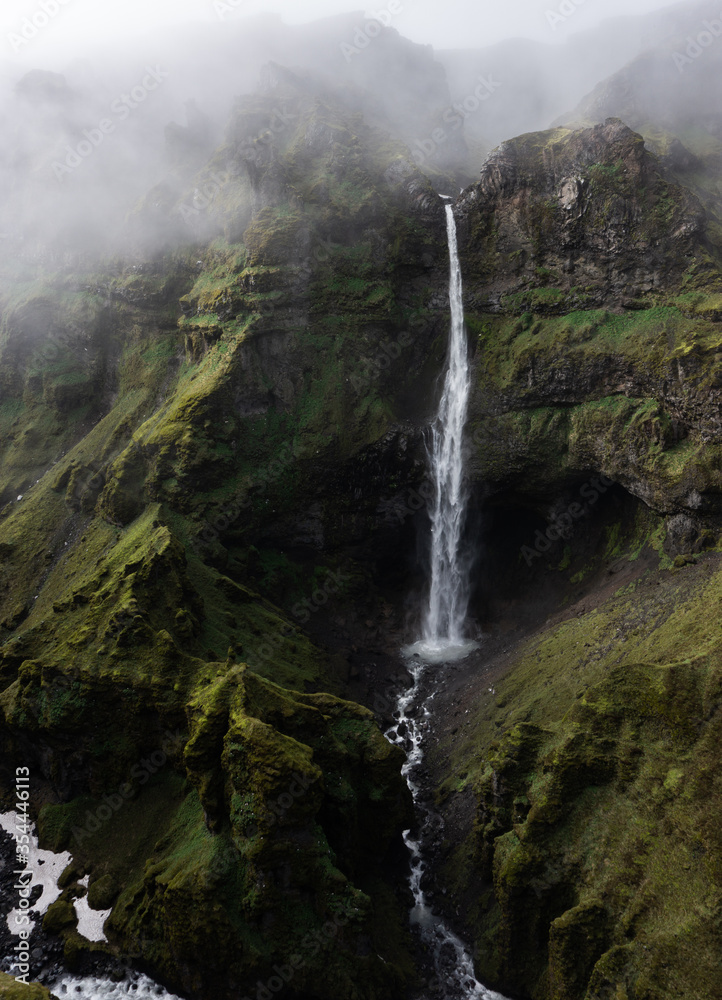 A magnificent waterfall in a dramatic canyon in Iceland on a foggy day.