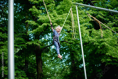 The girl is jumping on a bungee trampoline. A child with insurance and stretchable rubber bands hangs against the sky. The concept of happy childhood and games in the amusement park