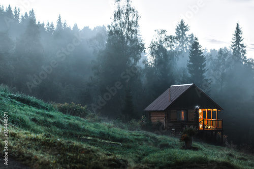 Small old wooden house in foggy forest. Mountains scenery. Nature conceptual image.