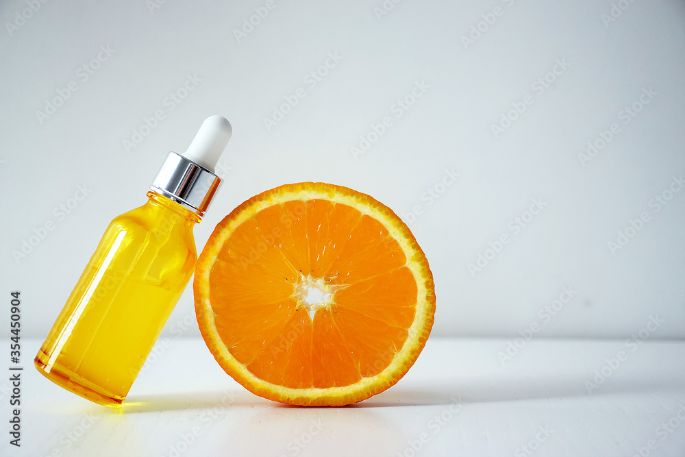 Cosmetic bottle with Vitamin C serum and half of orange on white background. Citrus essential oil, cosmetics aromatherapy. Organic SPA cosmetics with herbal ingredients.