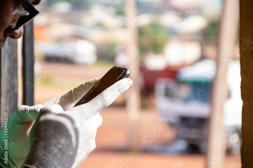 close up of young african man wearing a surgical gloves, post covid-19 living, using a mobile phone, texting